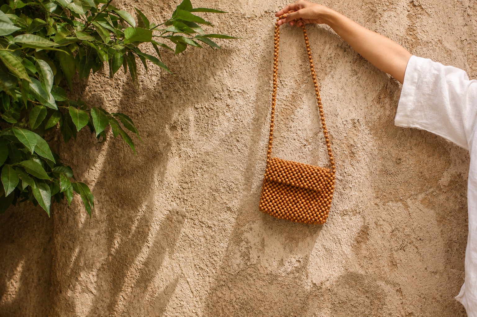 A natural wooden beaded bag held in warm sunlight against a textured wall.