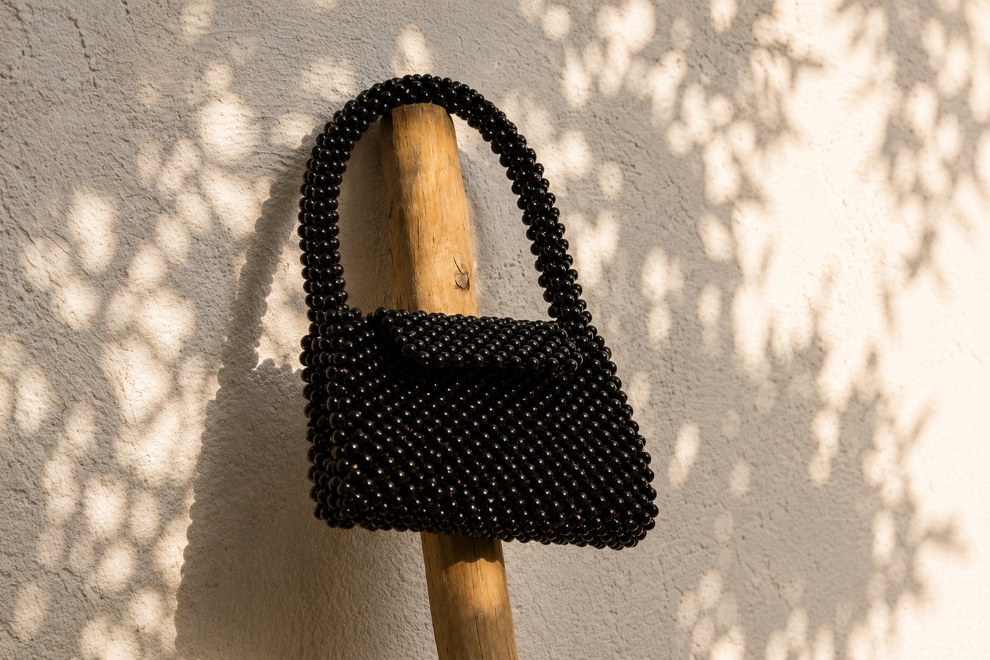 A dark structured beaded bag against a wall patterned by leaf shadows.