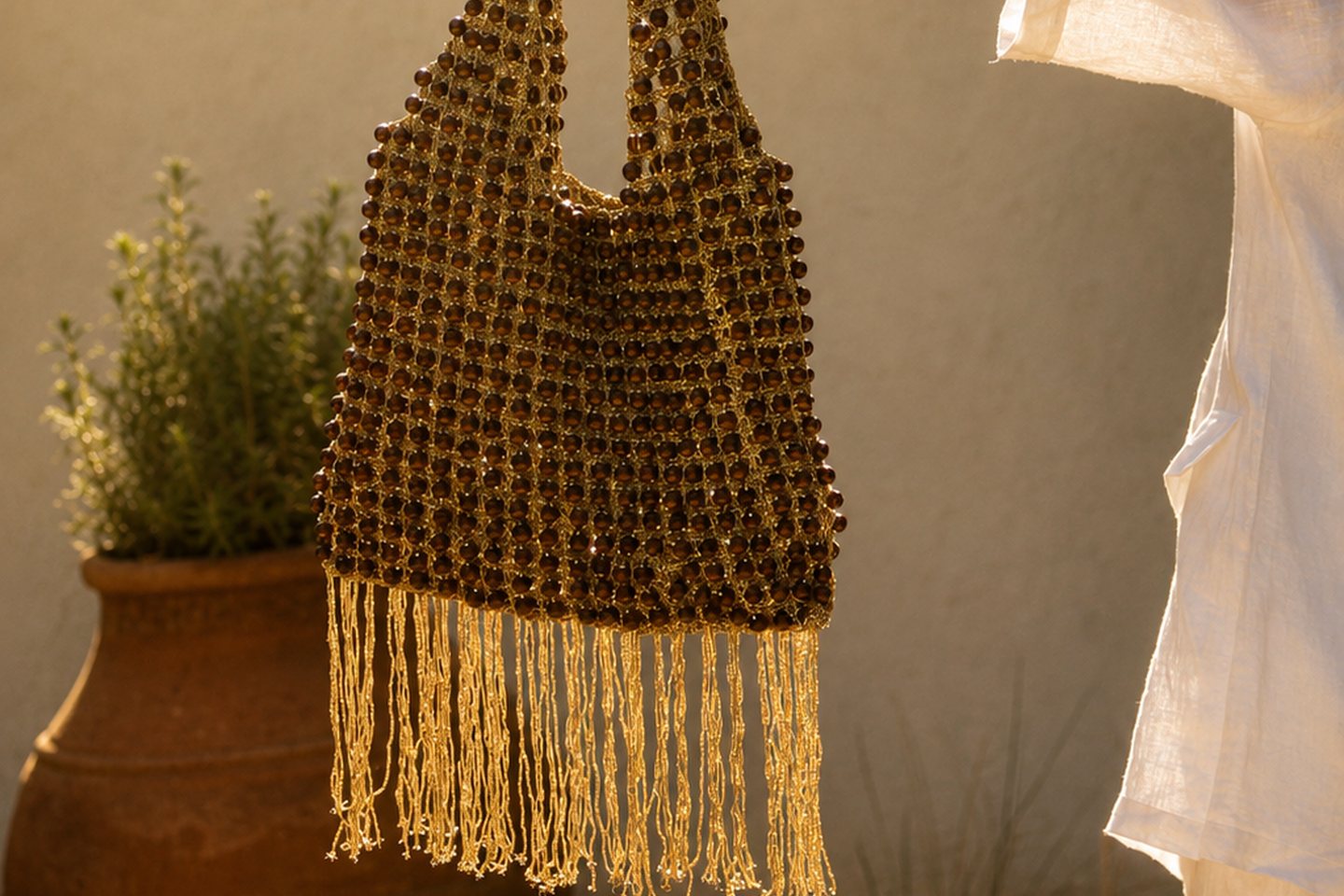 A fringed beaded bag held at body scale in warm evening light.