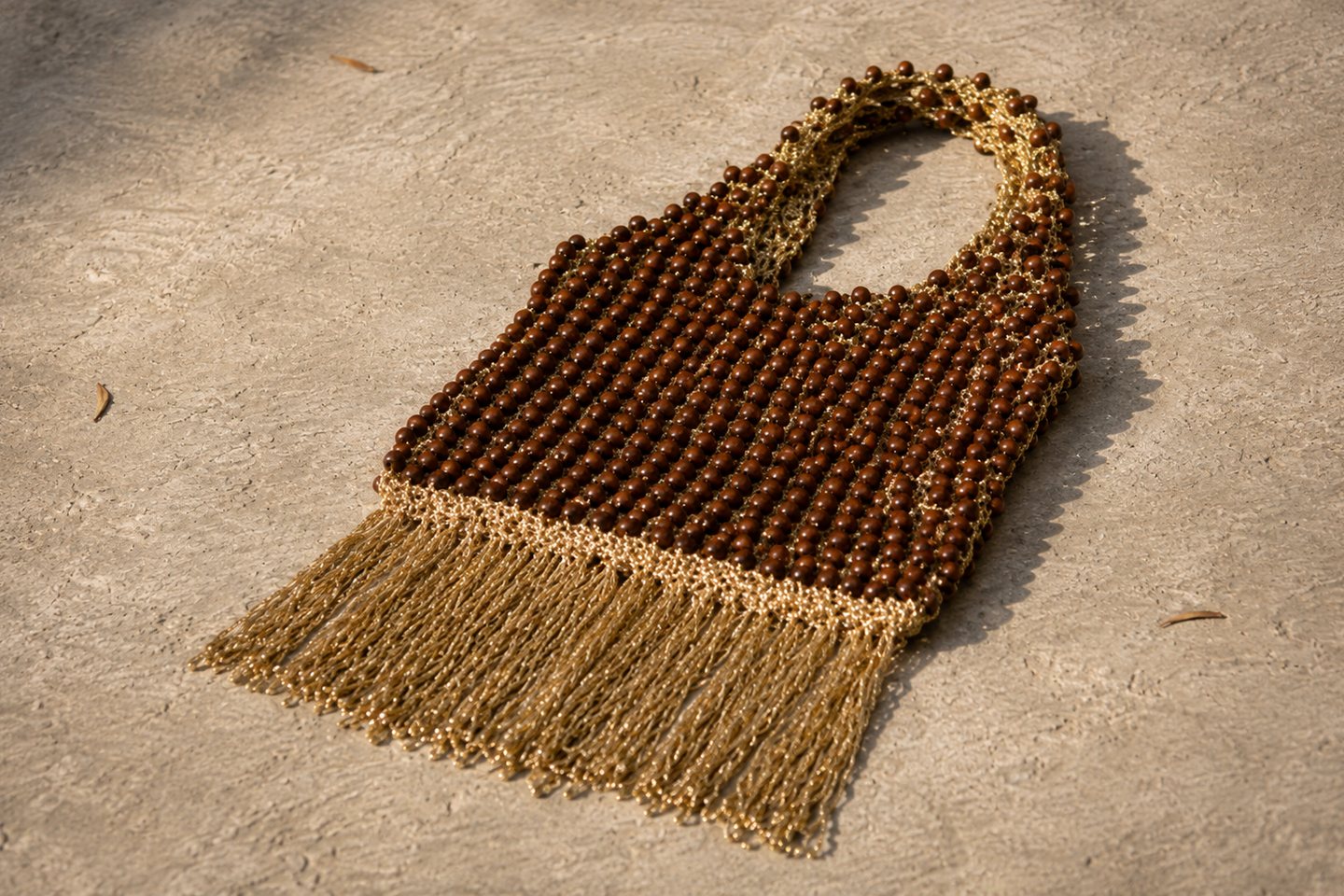 A fringed brown beaded bag seen from above on pale stone.