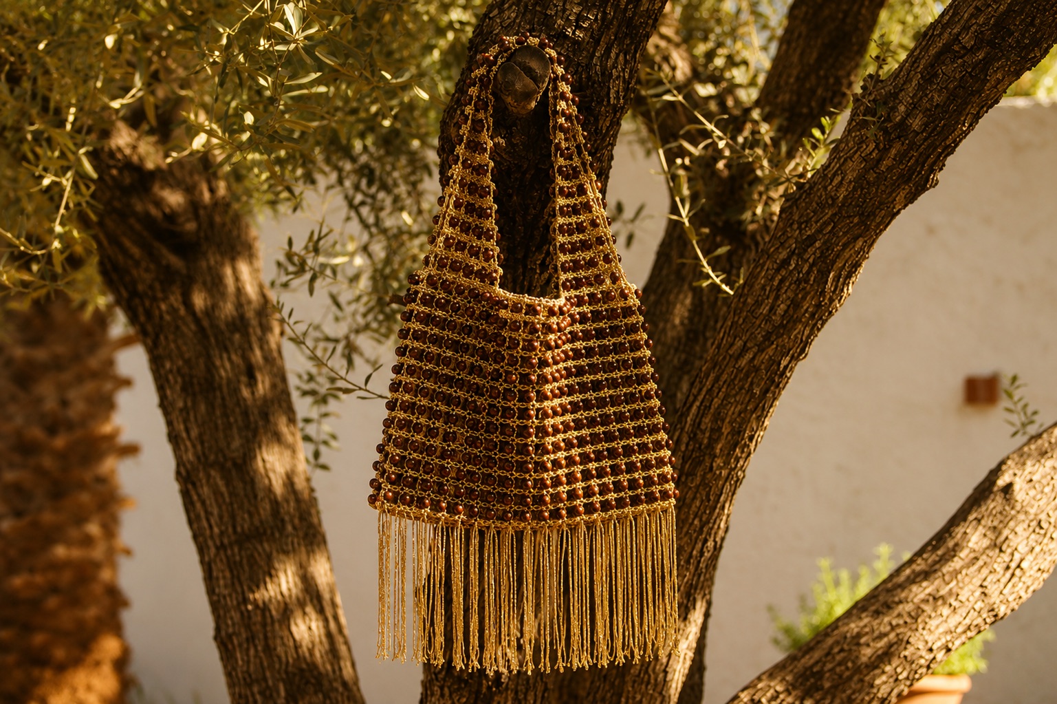 A long fringed beaded bag hanging from an olive tree in warm light.