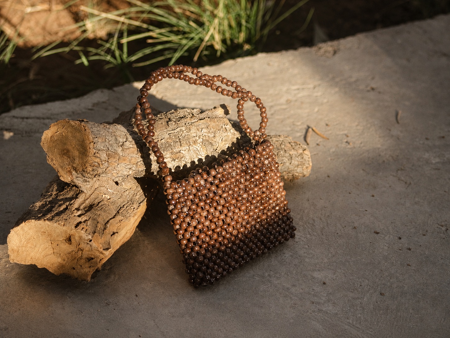 A handcrafted round beaded bag resting on weathered wood and stone.
