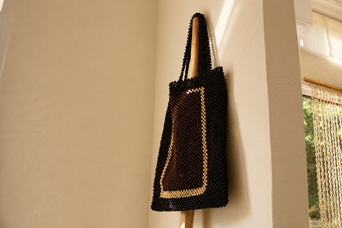 A dark beaded tote hanging in a calm sunlit interior.