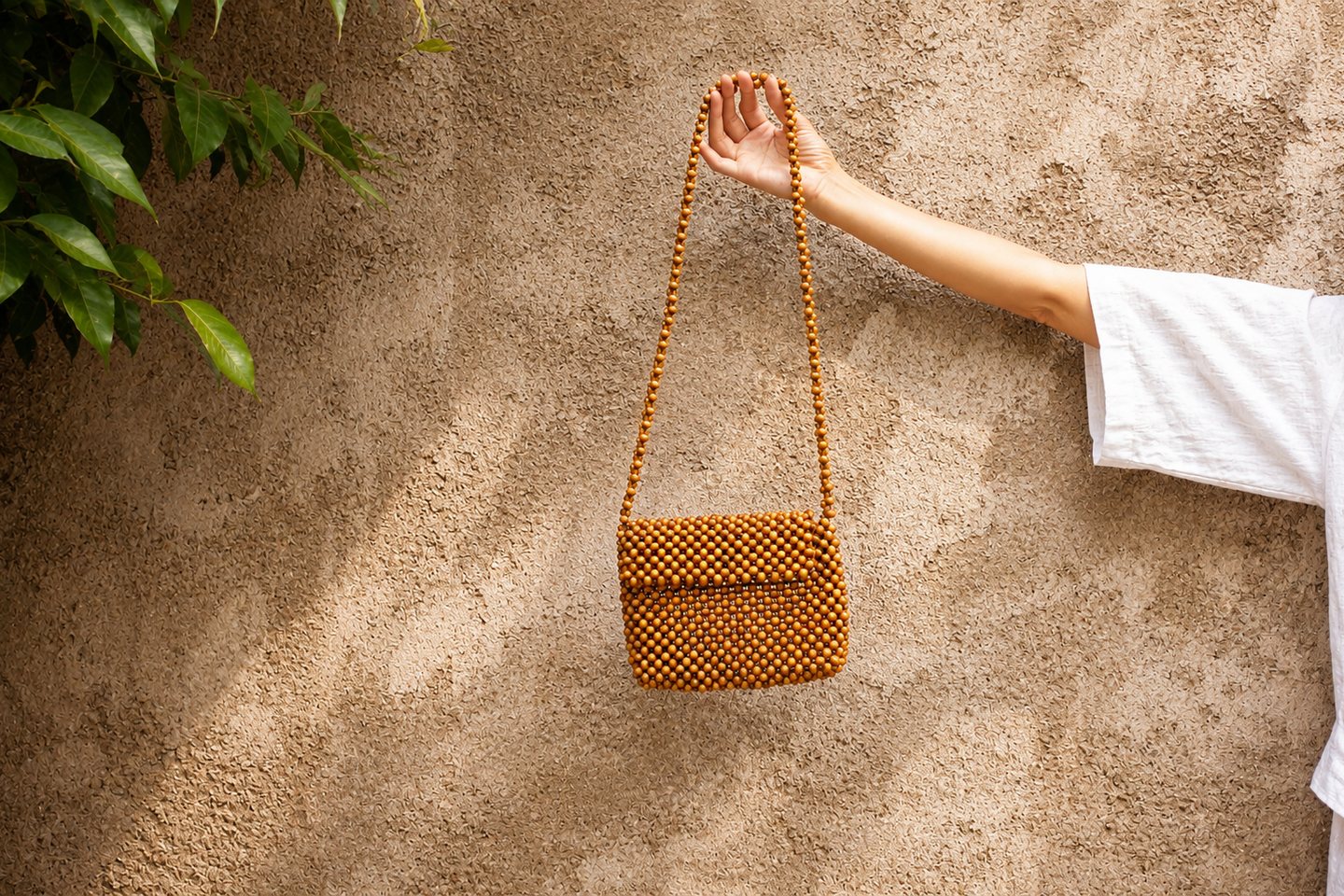 A white sleeve and handcrafted bag crossing a warm textured wall.
